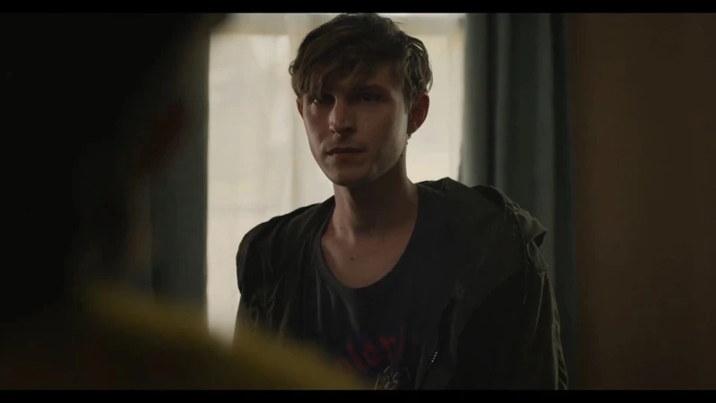 Portrait of a young adult male in a casual outfit, looking towards the left side of the frame indoors with a neutral expression.