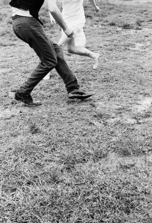 Monochrome action shot of a man and a barefoot woman running across a grassy field by Carter Smith.