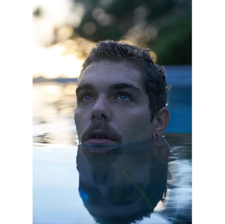 Close-up portrait of a man submerged up to his chin in water, with a clear reflection visible below the surface.