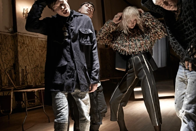 Group of four models posing in an indoor hall with stacked wooden chairs, captured by photographer Carter Smith.