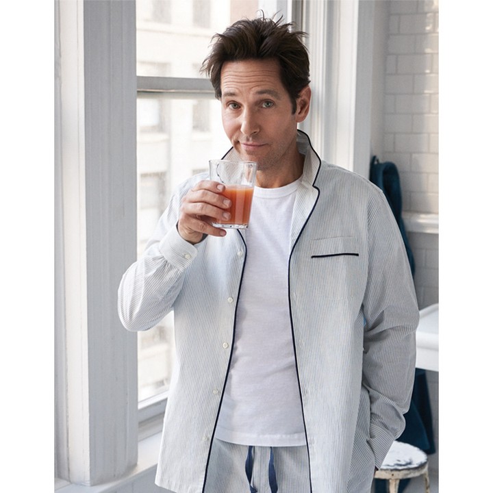 Indoor studio shot of a man in striped pajamas drinking a beverage near a window, showcasing casual style and a relaxed lifestyle.