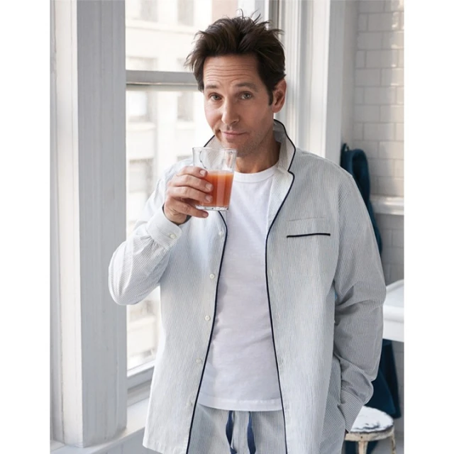 Indoor studio shot of a man in striped pajamas drinking a beverage near a window, showcasing casual style and a relaxed lifestyle.