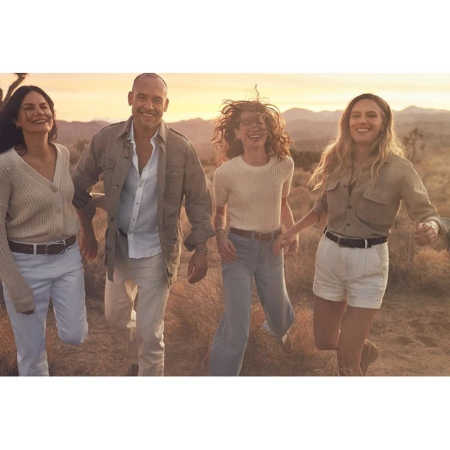 Four people smiling and walking outdoors in a desert landscape, with a warm color grade creating a cheerful and adventurous mood.