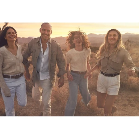 Four people smiling and walking outdoors in a desert landscape, with a warm color grade creating a cheerful and adventurous mood.
