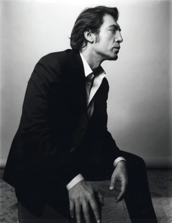 Portrait of a middle-aged man wearing a black suit and white shirt, seated indoors, looking off to the side in a black and white photograph.