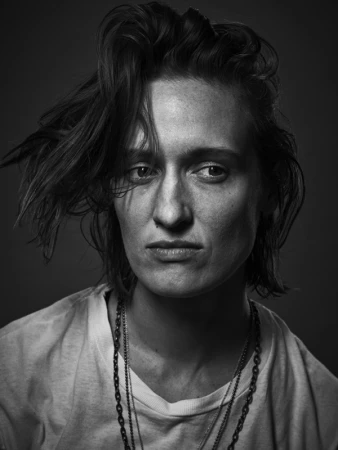 Monochrome portrait of a person with tousled hair wearing a white t-shirt and layered chain necklaces by Justin Stephens