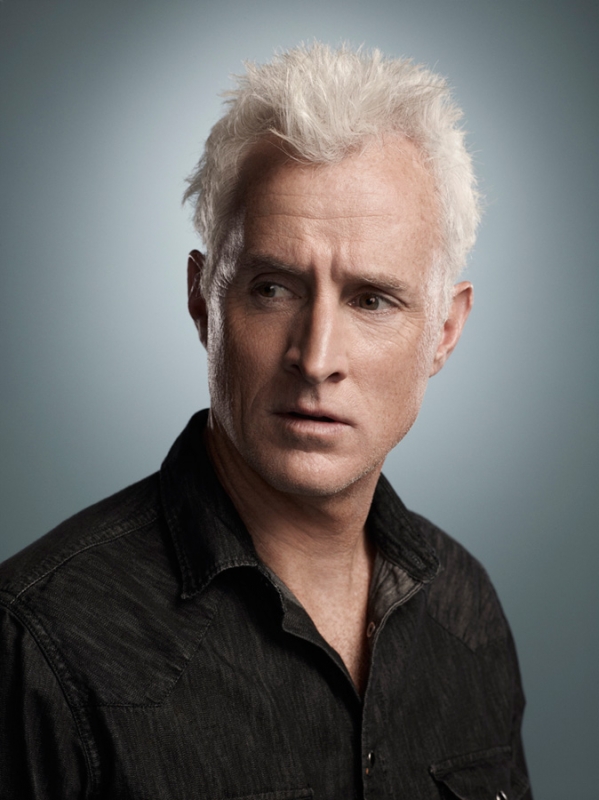 Justin Stephens portrait of a male model in a photo studio with gray backdrop, studio lights, and makeup artist touching up face.