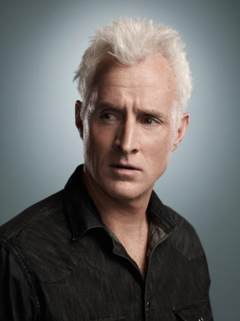 Justin Stephens portrait of a male model in a photo studio with gray backdrop, studio lights, and makeup artist touching up face.