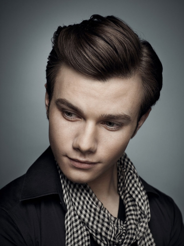 Headshot of a fair-skinned adult male with styled dark hair wearing a black collared shirt and black-and-white scarf, against a grey backdrop.