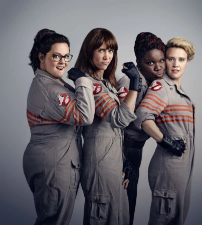 Four women in 'Ghostbusters' jumpsuits posing in a photo studio, smiling and looking at the camera with a grey background.