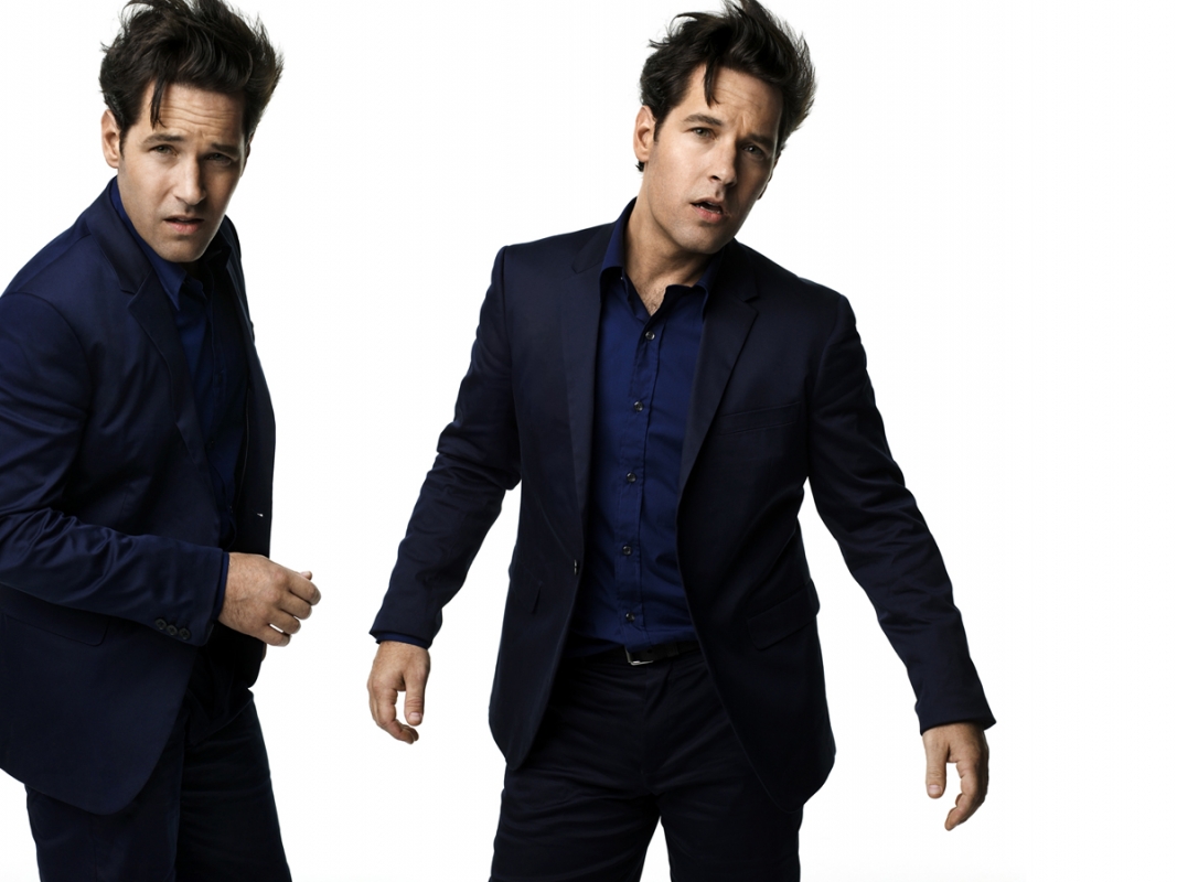 Studio portrait of Paul Rudd wearing a navy suit and blue shirt, posing against a white background, duplicated in the frame.