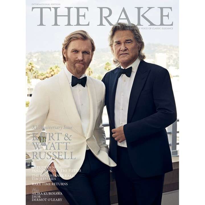 Magazine cover featuring two adult men in tuxedos: Kurt Russell and Wyatt Russell, standing outdoors with a blurred city background.