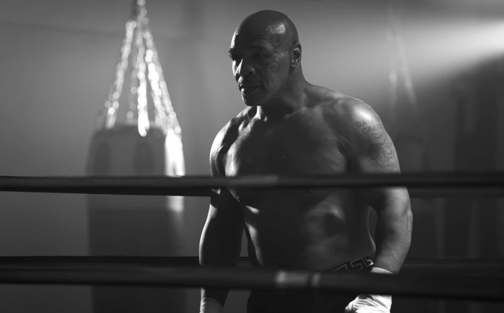 Black and white portrait of Mike Tyson in a boxing ring with a hanging punching bag in the background