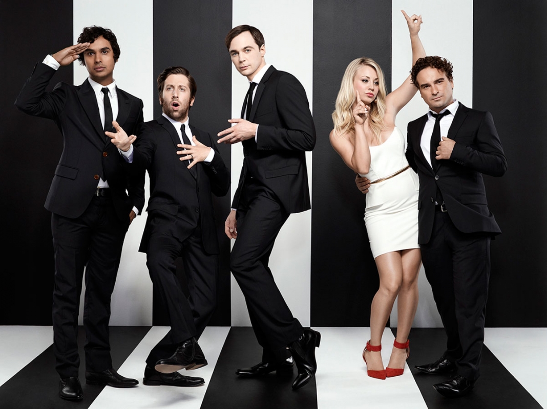Group photo of five 'The Big Bang Theory' cast members posing in black suits and formal wear against a black and white stripe backdrop.
