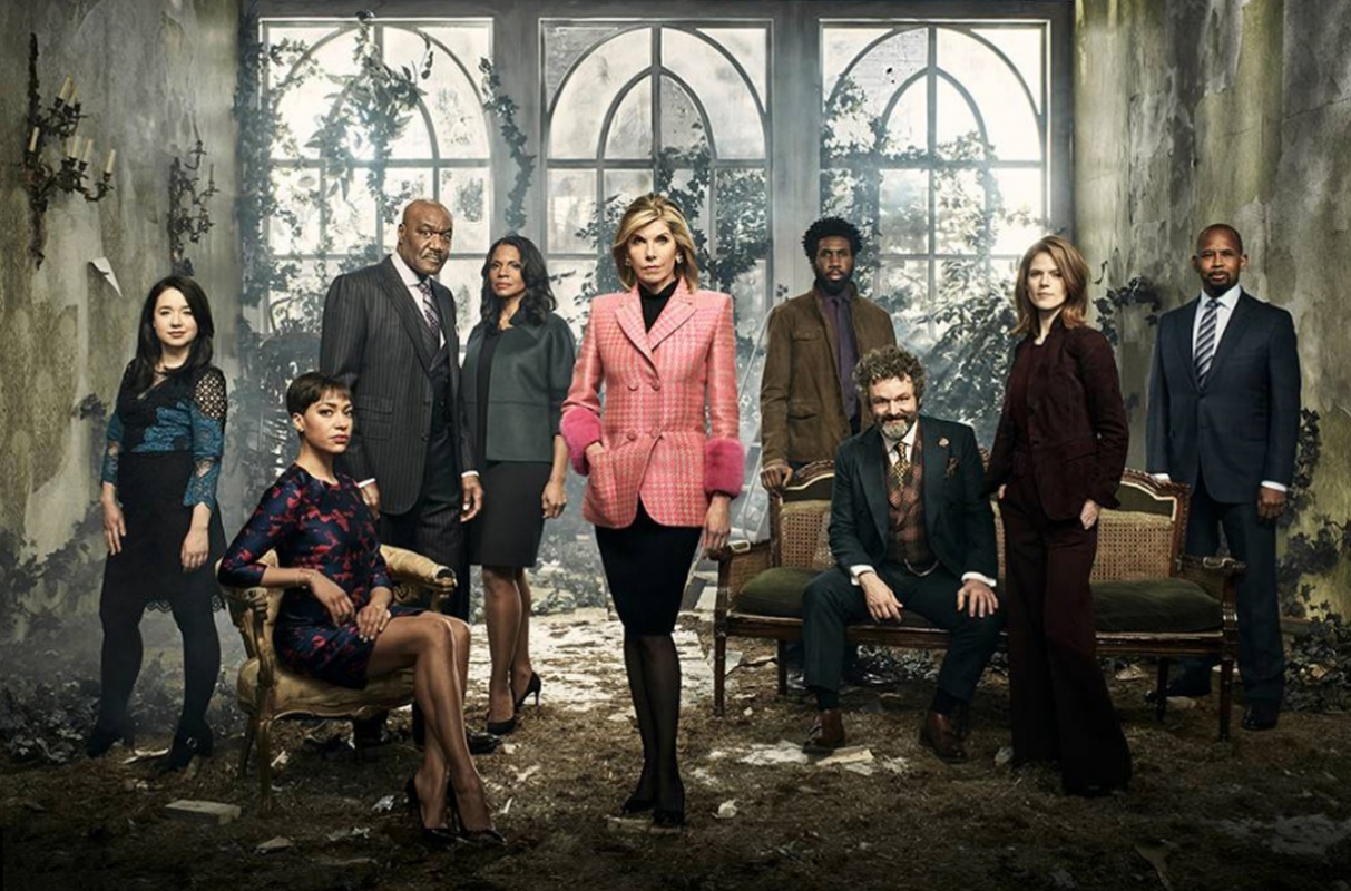 Group of diverse adult actors and actresses in formalwear pose for a promotional shot in an overgrown indoor set with large windows.
