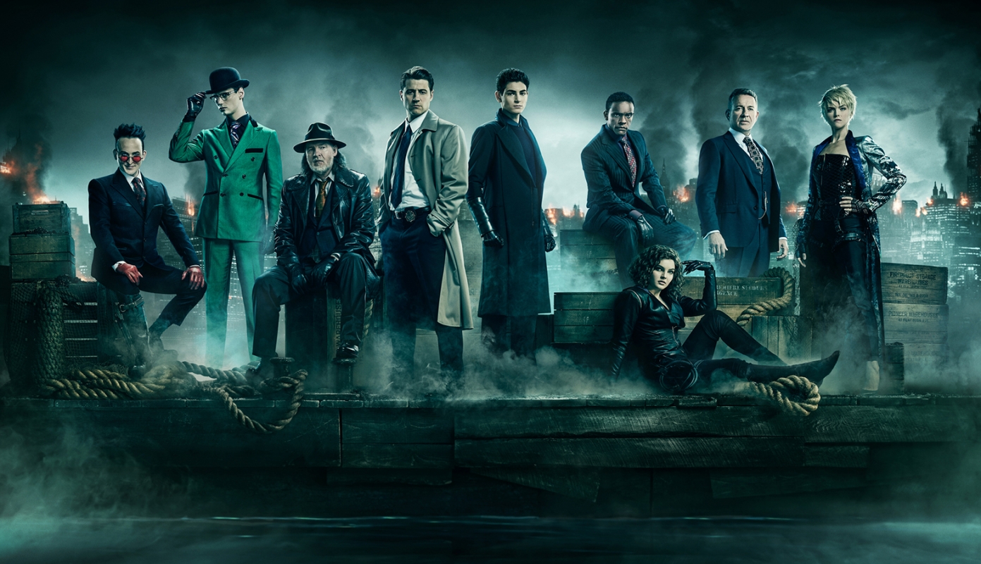 Group portrait of nine figures in formal wear, standing in a foggy urban setting with tall buildings in the background at night.