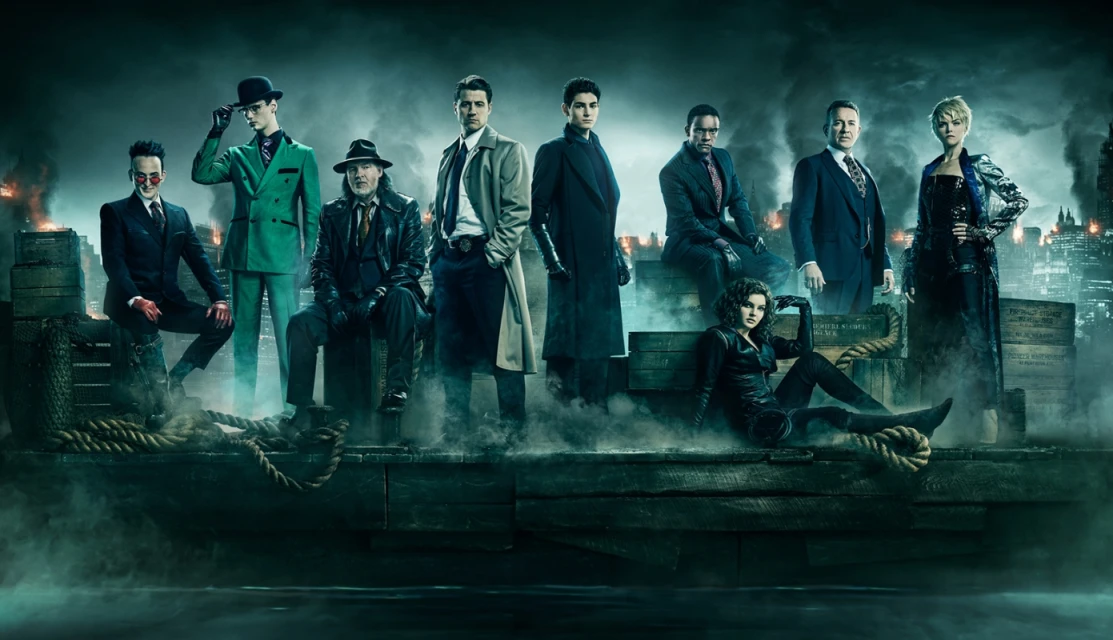 Group portrait of nine figures in formal wear, standing in a foggy urban setting with tall buildings in the background at night.