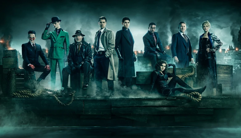 Group portrait of nine figures in formal wear, standing in a foggy urban setting with tall buildings in the background at night.