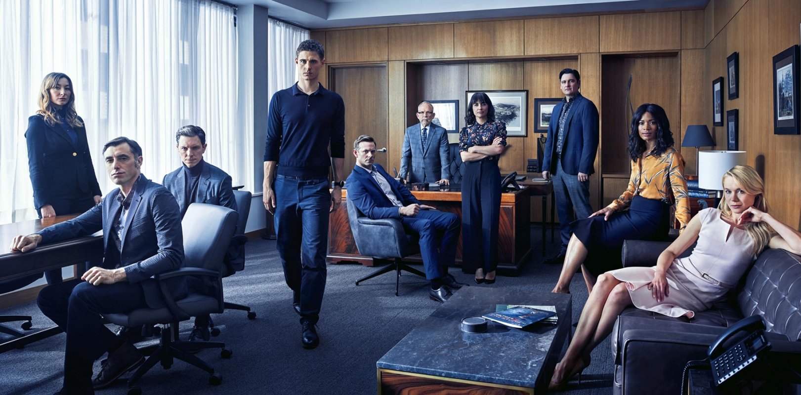 Group photo of nine people in a modern office with wood-paneled walls, neutral tones, and contemporary furniture, creating a professional atmosphere.