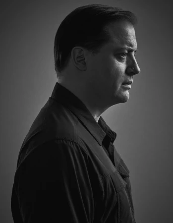 Portrait profile of Brendan Fraser in a dark collared shirt against a grey background photographed by Justin Stephens.