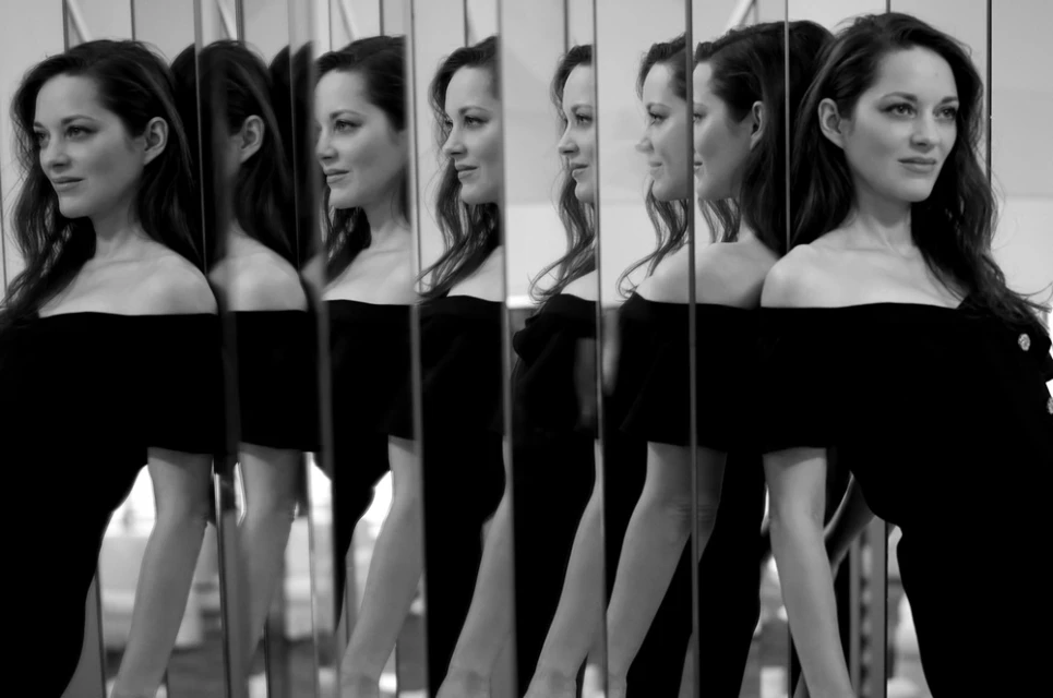 Black and white photo of a woman in a black dress, looking to the side, with multiple mirror reflections.