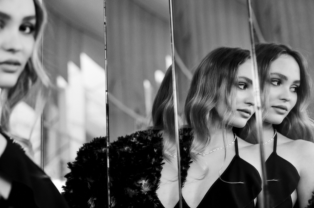 Portrait of a woman reflecting in a paneled mirror, showcasing her black top and necklace in a black and white medium shot.