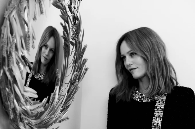 Portrait of Stella McCartney wearing a dark embellished top, captured in monochrome with her reflection in a decorated circular mirror.