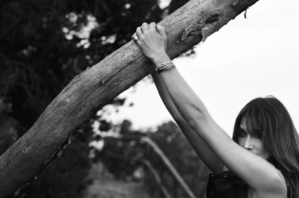 Black and white portrait of a woman holding onto a fallen tree branch outdoors with soft, diffused lighting.