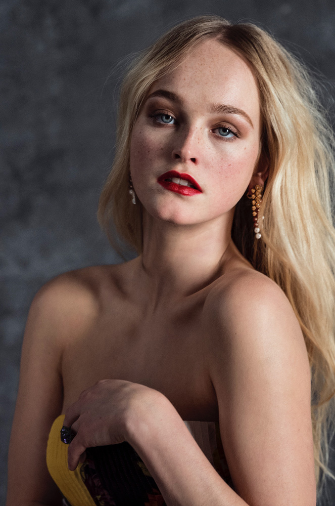 Blonde woman with red lipstick and jeweled earrings poses in front of a mottled gray background in a glamour portrait. Head and shoulders.