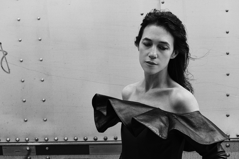 Monochrome portrait of a woman in a ruffled top against a riveted metal background, looking down with wet hair in a studio setting.