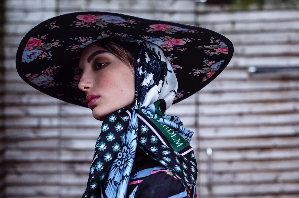 Portrait of a woman in a floral hat and patterned scarf, captured in a studio setting with soft, diffused lighting, showcasing fashion and beauty.