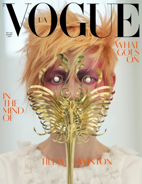 Vogue UA magazine cover featuring Tilda Swinton with golden hair, decorative golden mask, and pale skin, set against a bright background.