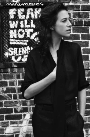 Portrait of Charlotte Gainsbourg in profile wearing a dark shirt against a brick wall by Anton Corbijn.