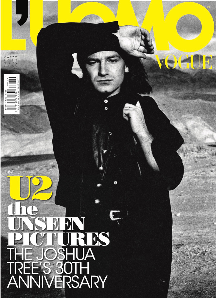 Bono on a L'Uomo Vogue cover. He is wearing a black shirt and jacket, with mountains in the blurred background.