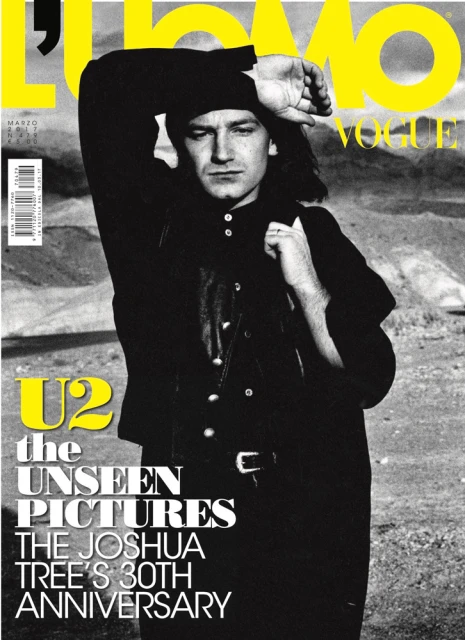 Bono on a L'Uomo Vogue cover. He is wearing a black shirt and jacket, with mountains in the blurred background.
