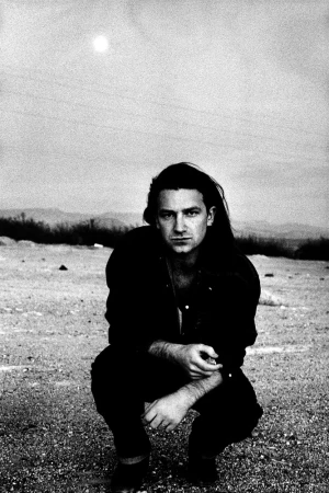 Anton Corbijn portrait featuring a male musician with dark hair wearing a black suit and tie, set against a textured background.