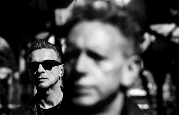 Monochrome portrait featuring a man in sunglasses with another blurred male figure in the background, evoking a music or celebrity aesthetic.
