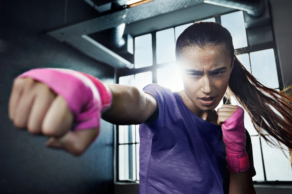 Athletic woman trains with pink hand wraps in a gritty indoor gym setting. Intense focus, determination, and fitness. Purple top.