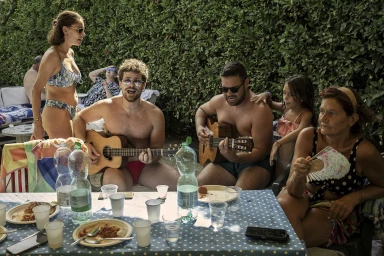 Candid outdoor gathering with two men playing guitars at a blue polka-dot table outdoors, captured by Karan Kapoor.