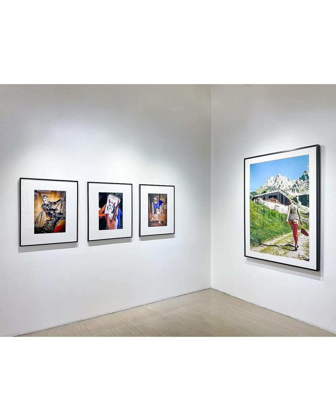 Art gallery exhibition featuring framed photographic prints displayed on white walls, showcasing different subjects and styles in a clean, modern space.