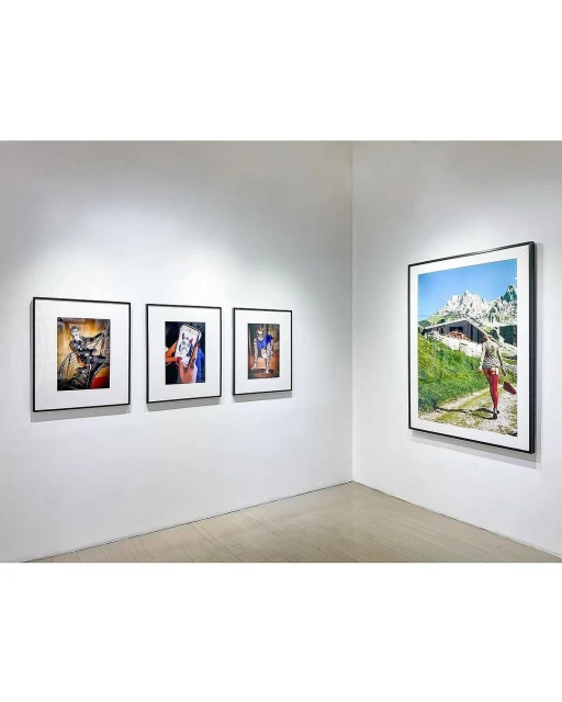 Art gallery exhibition featuring framed photographic prints displayed on white walls, showcasing different subjects and styles in a clean, modern space.