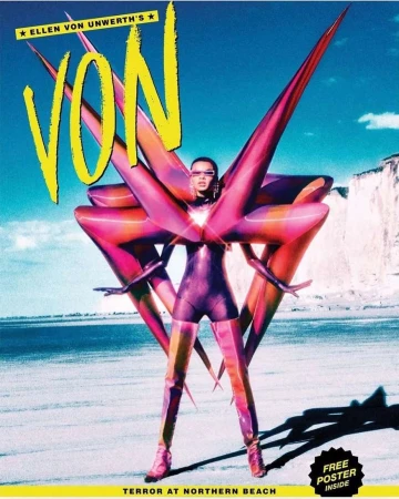 Magazine cover featuring a model in a body suit with an inflated structure, standing on a beach with rocky cliffs in the background.