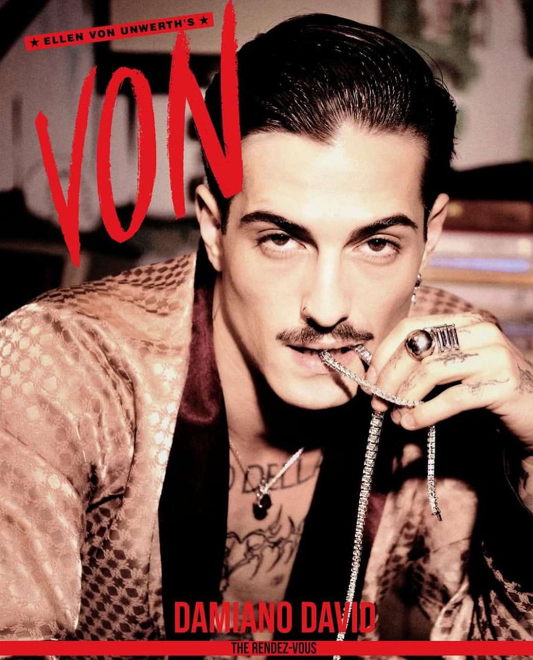 Damiano David portrait, eye-level view. He wears a patterned robe and jewelry, holding a diamond chain in his mouth. Red magazine type.