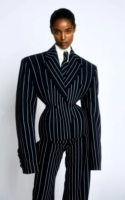 Fashionable African American woman in pinstripe suit with a narrow waist standing against a white backdrop in a studio setting.