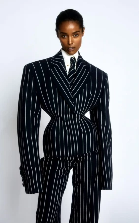 Fashionable African American woman in pinstripe suit with a narrow waist standing against a white backdrop in a studio setting.