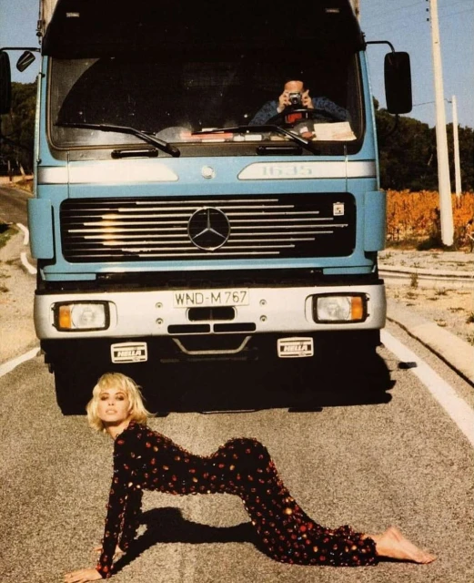 Fashion shot featuring a blond model in a sequined suit posing on an asphalt road with a blue Mercedes truck as a backdrop.