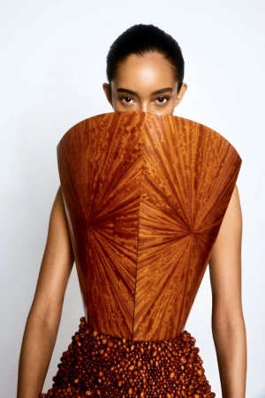 A woman models a wood-textured bodice with a beaded skirt against a bright white backdrop in a fashion photography studio.