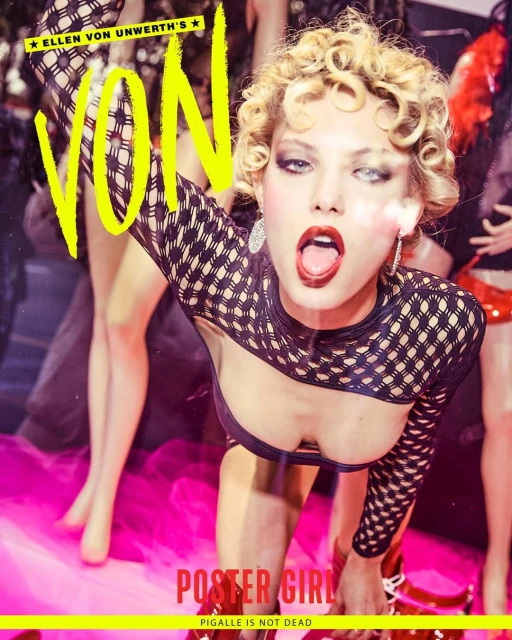 A blonde adult female poses wearing a black fishnet top in a photo shoot. The background includes magazine text and posed mannequins.