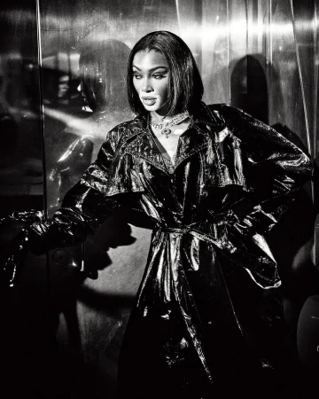 Black and white portrait of a woman wearing a shiny patent leather trench coat and necklace, shot by Ellen Von Unwerth.