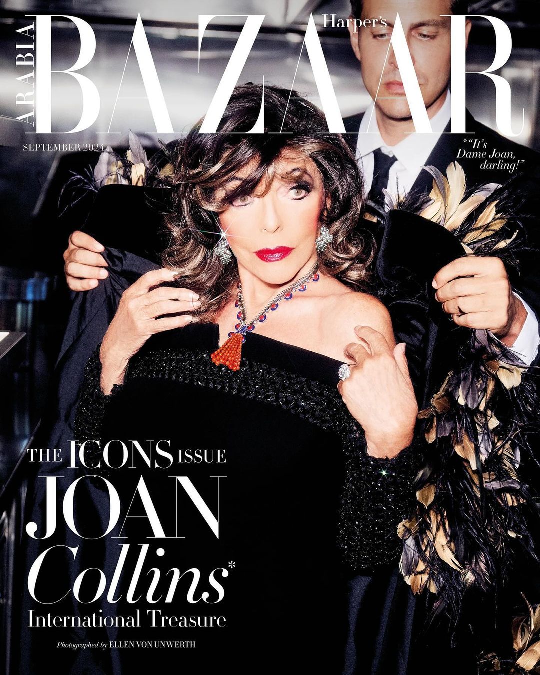 Joan Collins on Harper's Bazaar cover, September 2023. She wears a black dress and statement jewelry, with a man behind her.